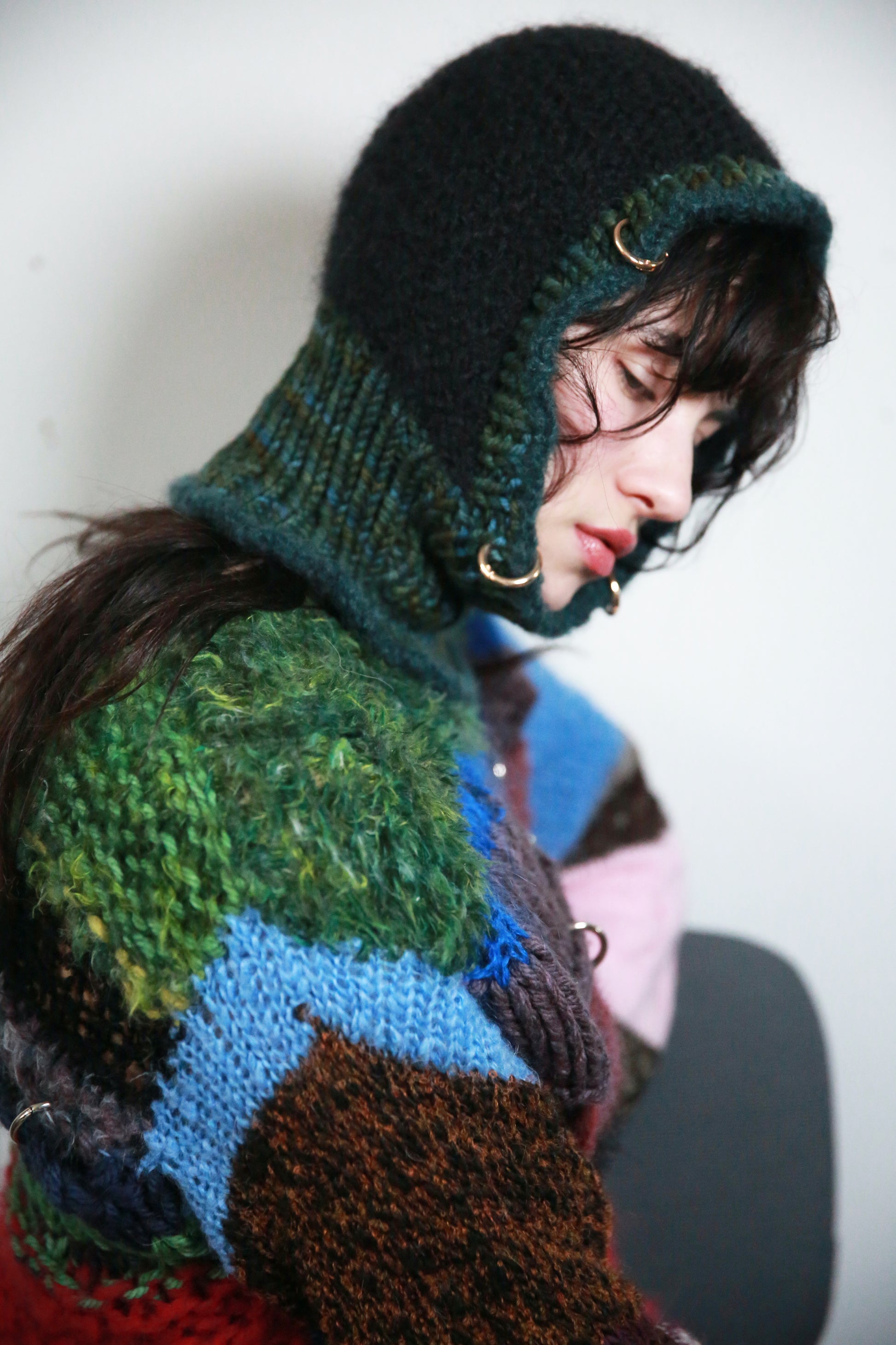 Person wearing a colorful knit sweater with a hood against a white background